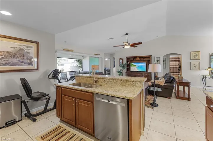Kitchen featuring dishwasher, a center island with sink, sink, vaulted ceiling, and light tile patterned floors