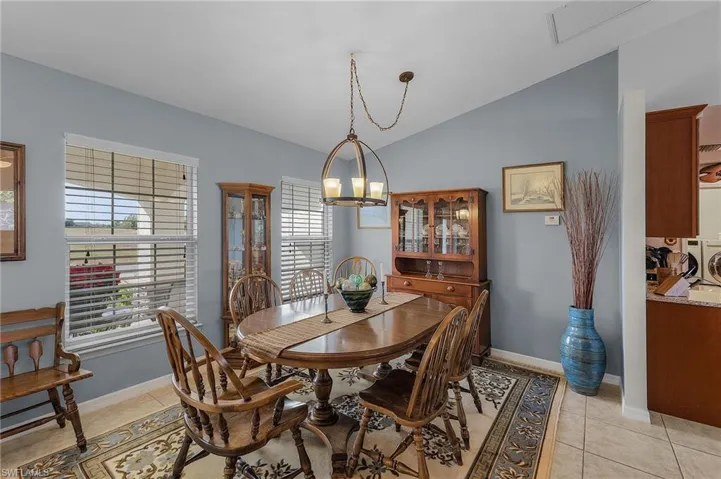 Dining room with lofted ceiling, independent washer and dryer, light tile patterned floors, and an inviting chandelier