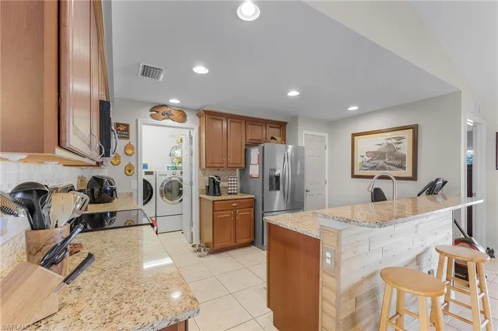 Kitchen with a kitchen breakfast bar, tasteful backsplash, light stone counters, separate washer and dryer, and stainless steel fridge