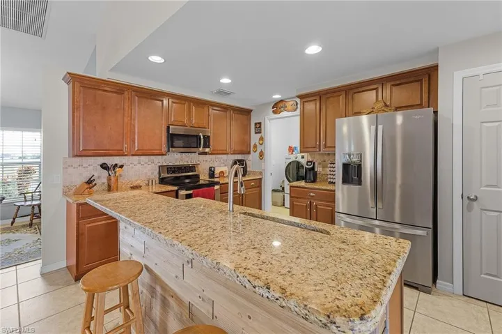 Kitchen featuring appliances with stainless steel finishes, a kitchen breakfast bar, light stone counters, light tile patterned floors, and washing machine and clothes dryer