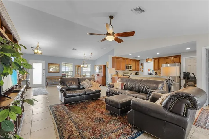 Living room featuring ceiling fan with notable chandelier, light tile patterned floors, and vaulted ceiling