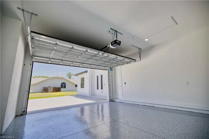 Spacious garage with an epoxy-coated concrete floor, an overhead garage door opener, and a ceiling-mounted access panel