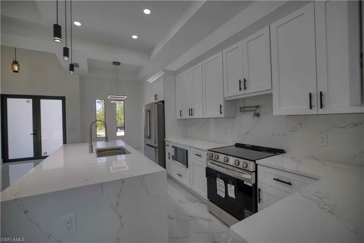 Modern kitchen featuring a large island with an undermount sink, white cabinetry with black hardware, stainless steel appliances, and a matching countertop and backsplash