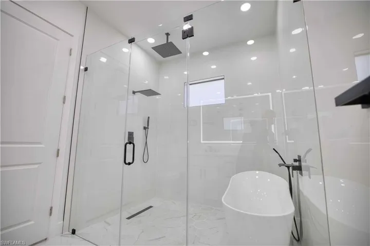 Contemporary bathroom featuring a frameless glass shower enclosure, a freestanding soaking tub with a floor-mounted matte black faucet, and hexagon tile flooring