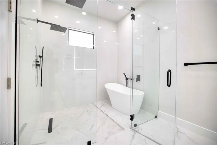 Contemporary bathroom featuring a spacious glass-enclosed shower, freestanding bathtub, rainfall showerhead, matte black fixtures, and marble-look tile flooring