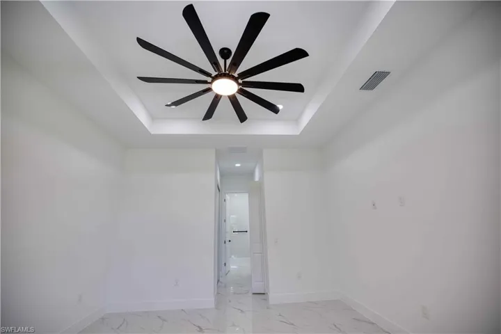Recessed ceiling feature with a large multi-blade ceiling fan, pristine white walls, and marble-look tile flooring