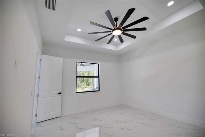 Tray ceiling with a modern ceiling fan and recessed lighting, white walls, and a window with a black frame