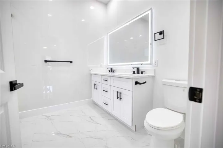Contemporary bathroom featuring a dual vanity with white cabinetry, black hardware, and a lighted mirror