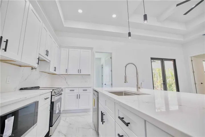Modern kitchen featuring white cabinetry with matte black hardware, stainless steel appliances, and a large island with an integrated sink
