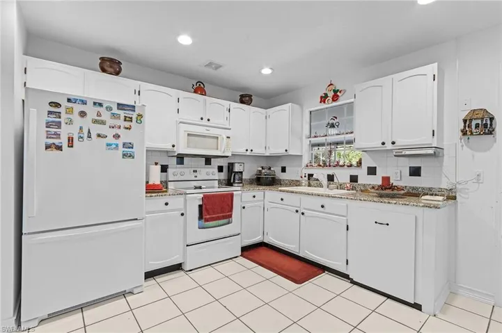 Kitchen with white cabinetry, sink, light stone countertops, tasteful backsplash, and white appliances