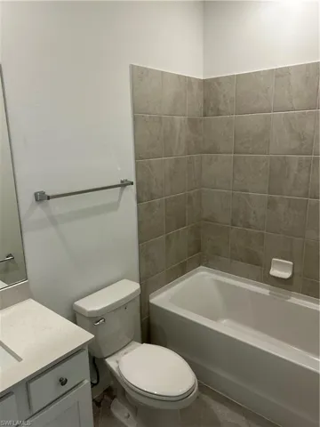 Full bathroom featuring a white porcelain tub, light-toned wall tiling, white vanity with integrated sink, and coordinating floor tiles