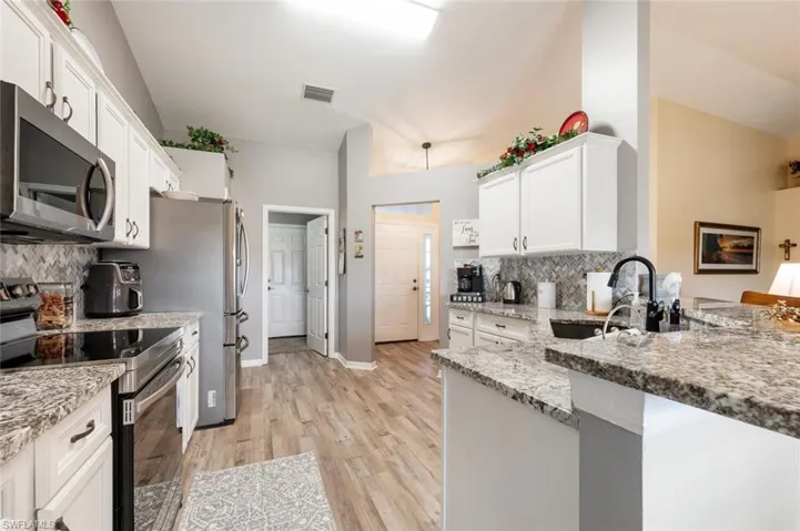 Kitchen featuring light wood-type flooring, stainless steel appliances, white cabinetry, backsplash, and sink