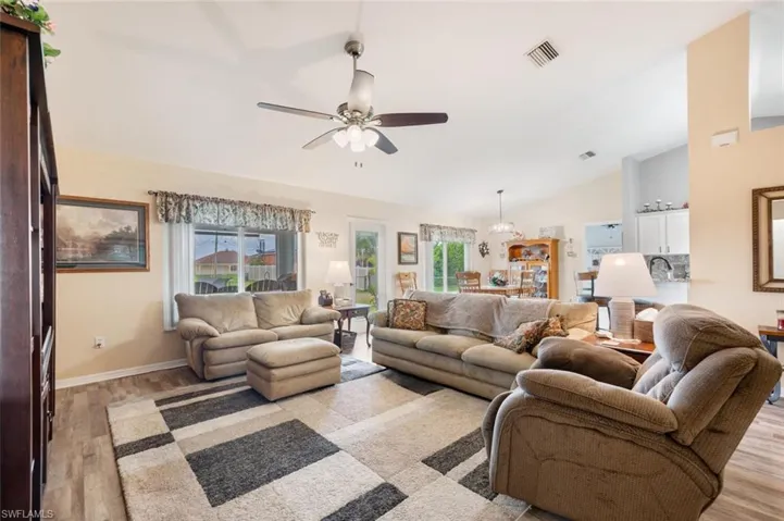Living room with ceiling fan with notable chandelier, vaulted ceiling, and light hardwood / wood-style floors
