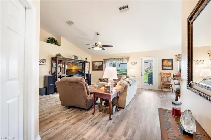 Living room with ceiling fan, light wood-type flooring, and vaulted ceiling