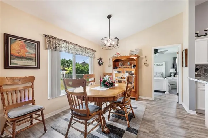 Dining space with light hardwood / wood-style flooring, ceiling fan with notable chandelier, and lofted ceiling