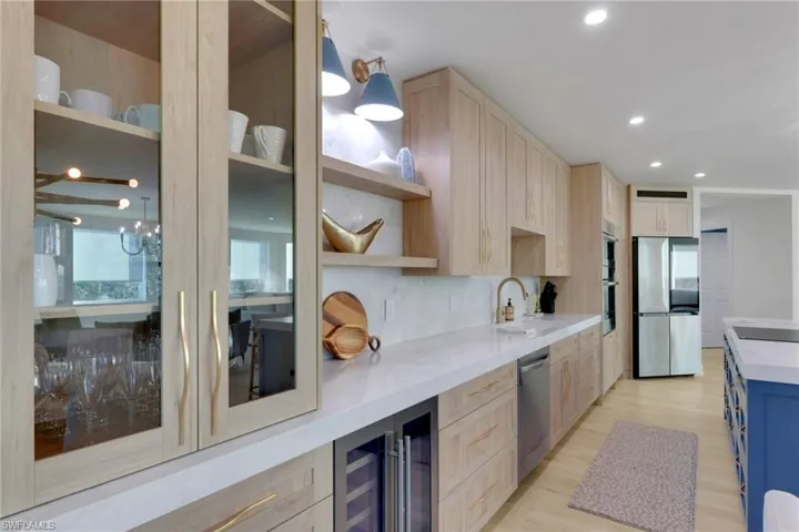 Kitchen with light brown cabinetry, light stone counters, beverage cooler, appliances with stainless steel finishes, and recessed lighting