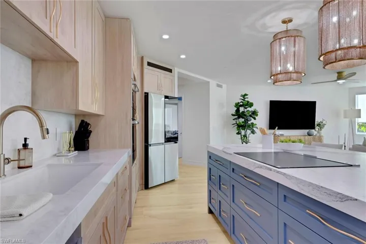 Kitchen with blue cabinets, light stone counters, recessed lighting, light wood finished floors, and hanging light fixtures