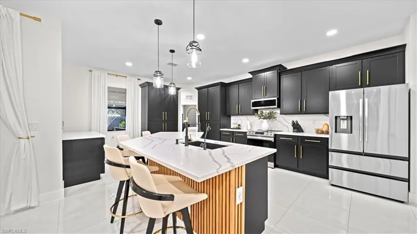 Kitchen featuring appliances with stainless steel finishes, dark cabinetry, light stone counters, hanging light fixtures, and light tile patterned floors