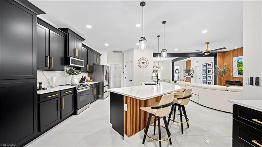 Kitchen with dark cabinets, hanging light fixtures, stainless steel appliances, light stone counters, and open floor plan