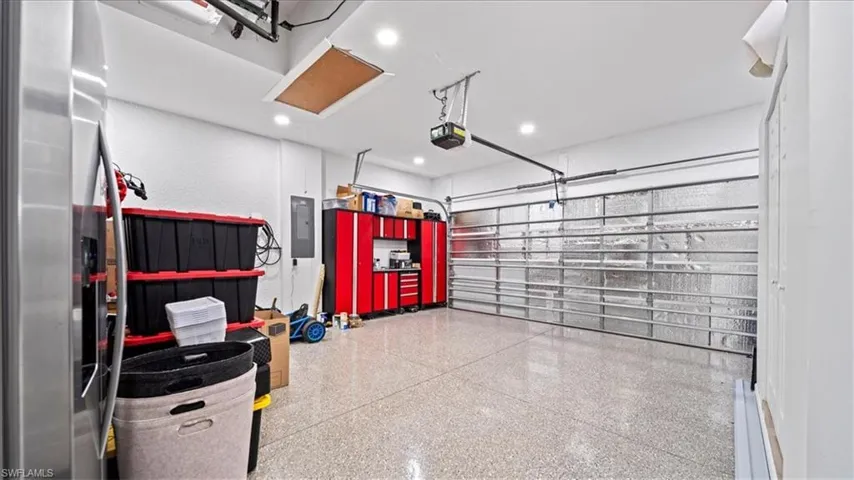 Garage featuring stainless steel fridge, electric panel, recessed lighting, and a garage door opener