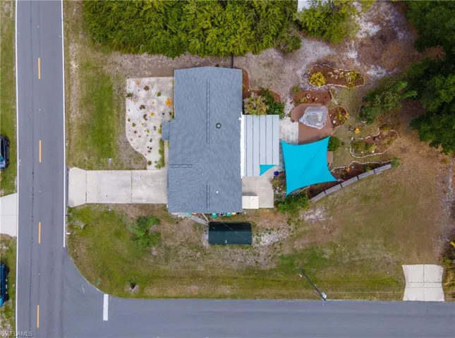 Overhead property perspective featuring a corner lot location, asphalt shingle roofing, concrete driveway, a blue shade sail, and landscaped rear yard areas