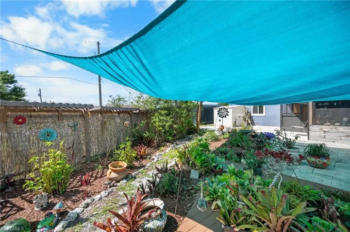 Landscaped backyard featuring a blue overhead shade sail, a bamboo fence, and a stone patio surface