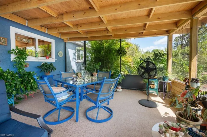 Screened patio featuring a wood-beam ceiling, textured flooring, and a blue stucco exterior wall with a white-framed window