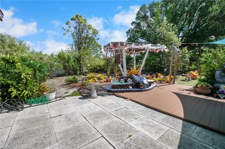 Expansive outdoor living area featuring a large paver patio, a curved wood-finish deck, a built-in pergola with decorative accents, and mature landscaping