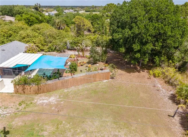Expansive backyard featuring a screened enclosure, a detached structure with a blue shade sail, a wood-panel fence, mature trees, and a landscaped garden