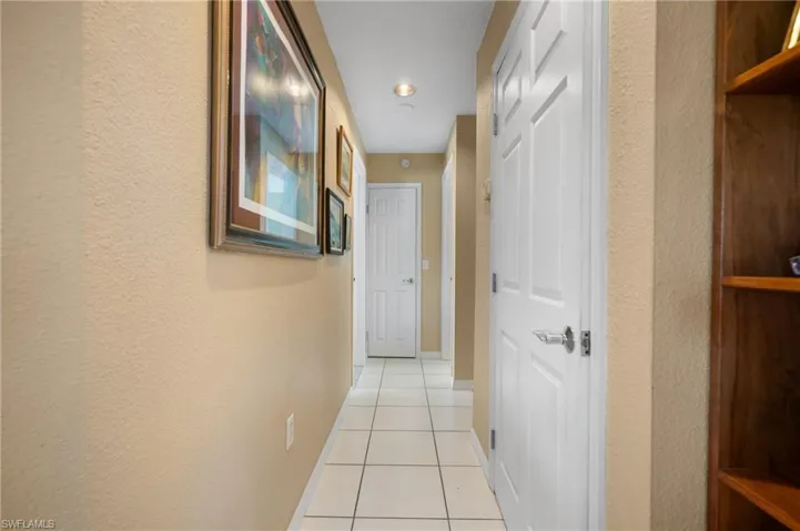 Hallway featuring neutral-toned walls, square white tile flooring, recessed ceiling lighting, and multiple paneled doors with chrome hardware