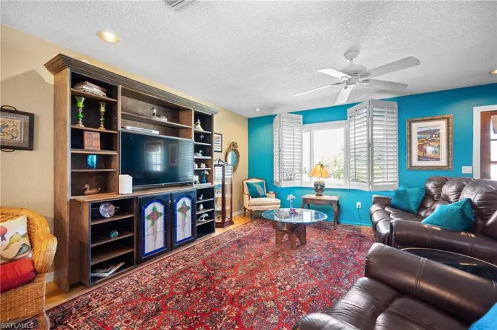 Spacious living area featuring a built-in entertainment center with integrated shelving, ceiling fan with light fixture, recessed lighting, and window with plantation shutters