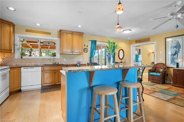Open-concept kitchen featuring wood-finish flooring, light wood cabinetry, a central island with a contrasting blue base, and stone-look countertops