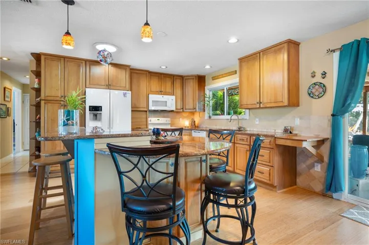 Spacious kitchen featuring wood-finish flooring, warm wood cabinetry, and a central island with a granite-style countertop