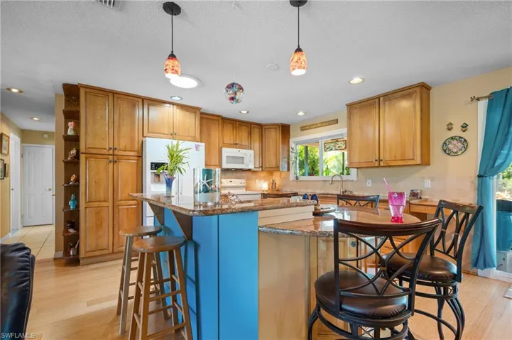 Kitchen featuring a central island with a contrasting blue base, granite countertops, and light-toned wood-finish flooring