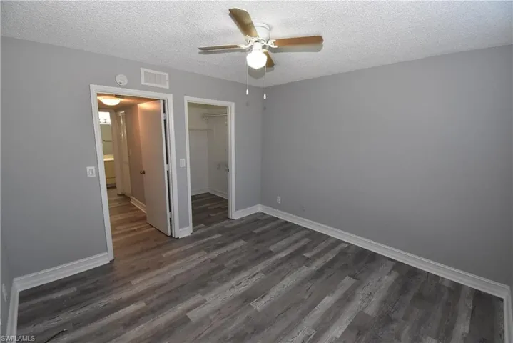Unfurnished bedroom featuring dark wood-style flooring, a spacious closet, a textured ceiling, and ceiling fan