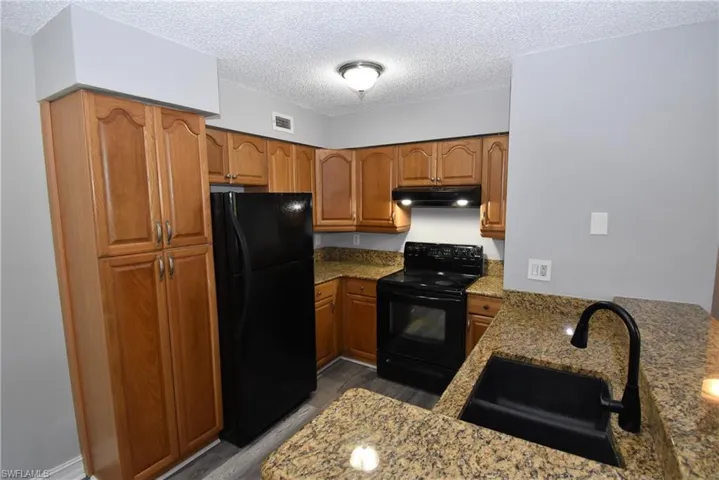 Kitchen with black appliances, wood finish cabinetry, light stone countertops, and a textured ceiling