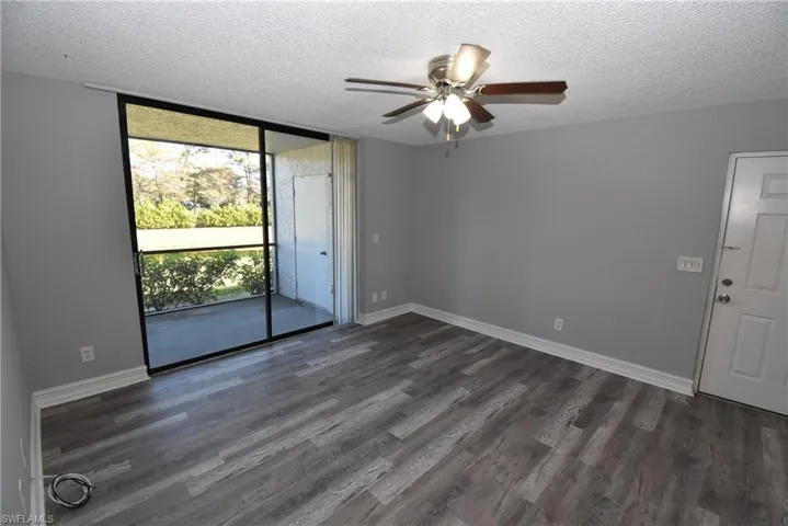 Empty room with expansive windows, ceiling fan, a textured ceiling, and dark wood finished floors