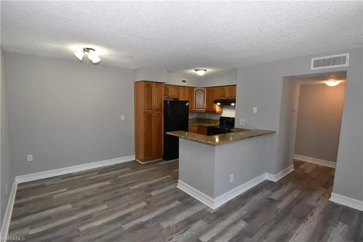 Kitchen featuring wood finish cabinets, black appliances, a peninsula, dark wood-style floors, and a textured ceiling