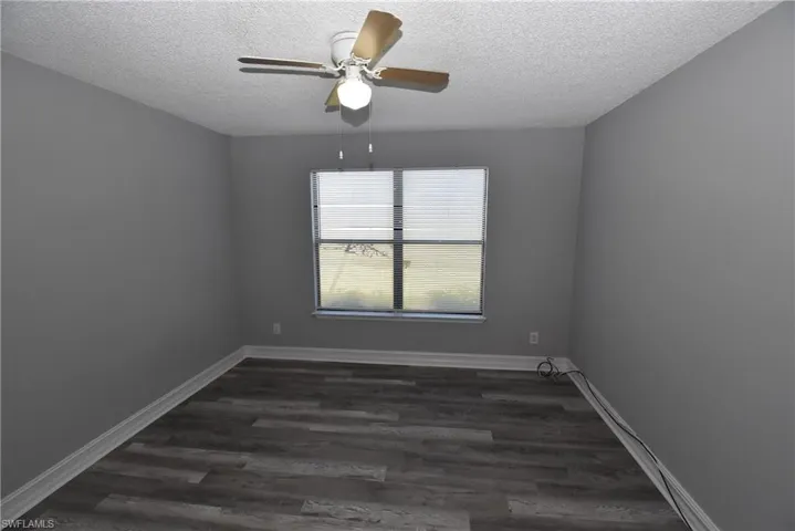 Unfurnished room featuring dark wood-type flooring, ceiling fan, and a textured ceiling