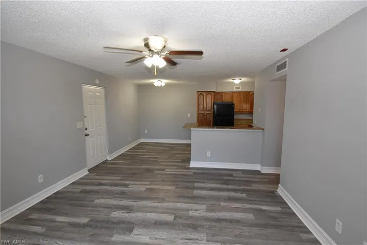 Unfurnished living room featuring a ceiling fan, dark wood finished floors, and a textured ceiling