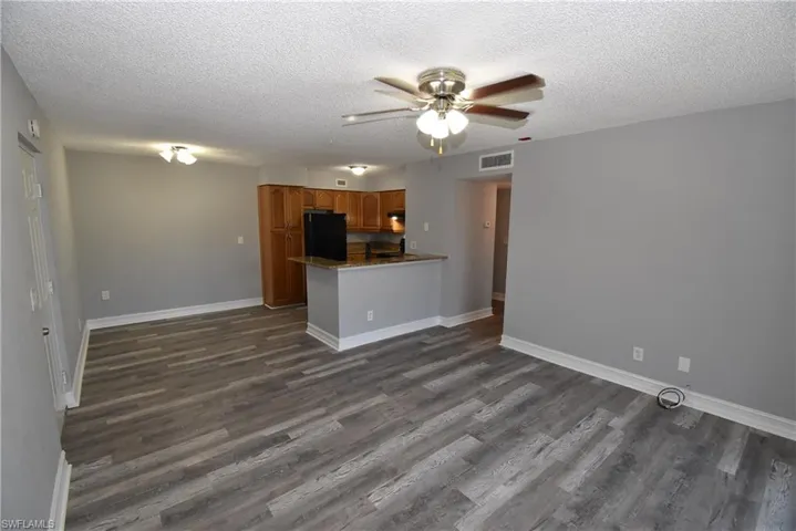 Kitchen with a ceiling fan, wood finish cabinets, freestanding refrigerator, a textured ceiling, and dark wood-style flooring