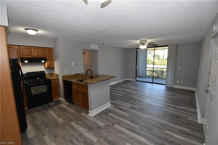 Kitchen with black appliances, a peninsula, open floor plan, wood finish cabinets, and a textured ceiling