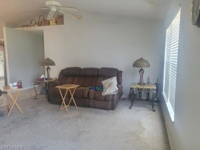 Carpeted living room with ceiling fan and lofted ceiling