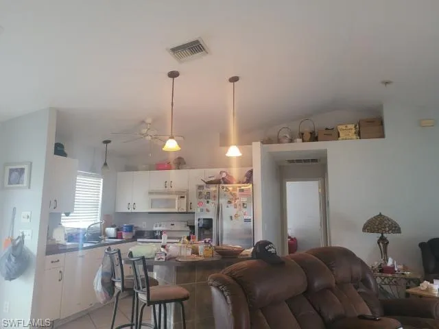 Kitchen with a kitchen breakfast bar, range, white cabinetry, stainless steel fridge, and lofted ceiling
