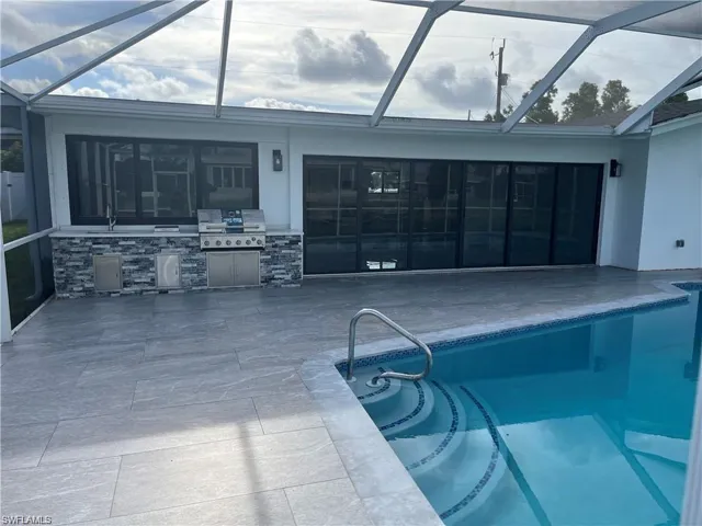 Swimming pool with a sunroom, a patio area, glass enclosure, and an outdoor kitchen