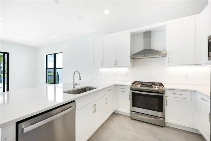 Kitchen with appliances with stainless steel finishes, sink, white cabinets, and wall chimney range hood