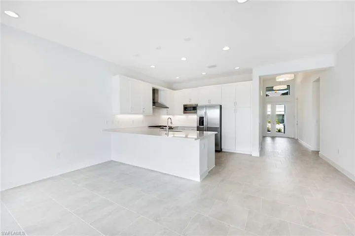 Kitchen with wall chimney exhaust hood, appliances with stainless steel finishes, kitchen peninsula, sink, and white cabinetry
