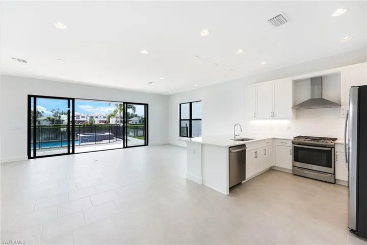 Kitchen featuring kitchen peninsula, appliances with stainless steel finishes, wall chimney exhaust hood, and white cabinetry
