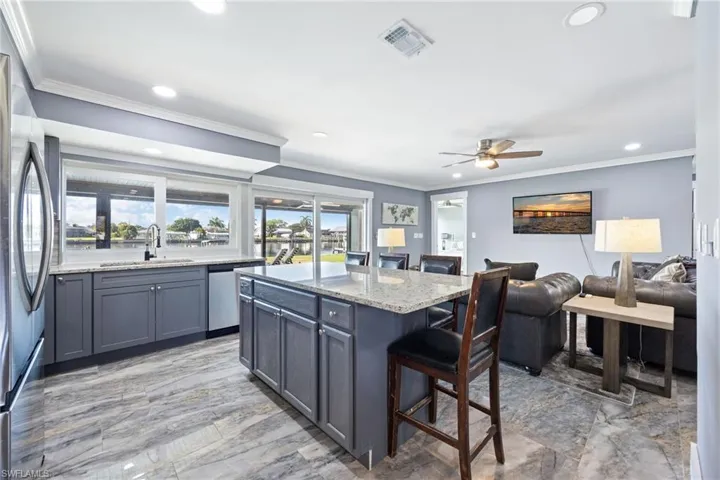 Kitchen with a breakfast bar area, light stone countertops, ornamental molding, stainless steel appliances, and a kitchen island