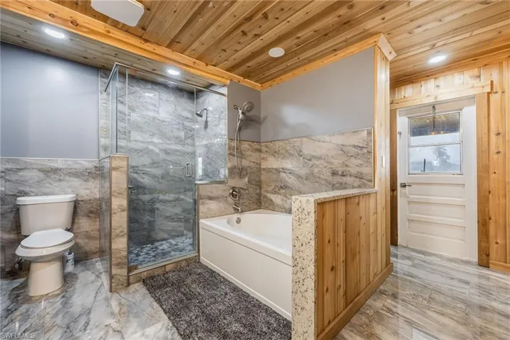 Full bath with light marble finish floors, a garden tub, a marble finish shower, tile walls, and a wainscoted wall